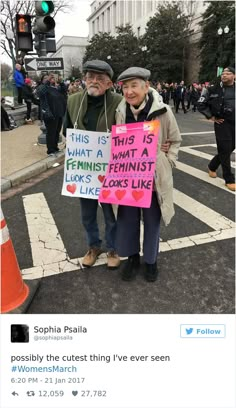 two people standing in the street holding signs that read this is what a feminist looks like