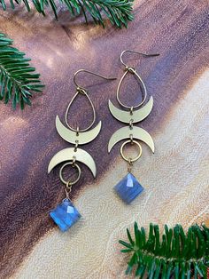 the moon and crescent earrings are on display next to some pine tree branches with green leaves