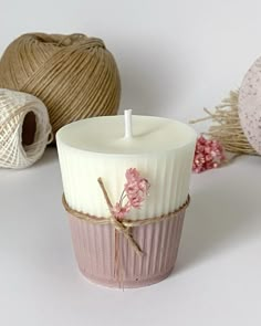 a white candle sitting on top of a table next to twine of yarn and flowers