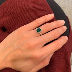 a woman's hand with a green ring on her finger and a red sweater