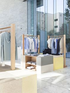 an open air clothing store with clothes on racks and shirts hanging in front of glass windows