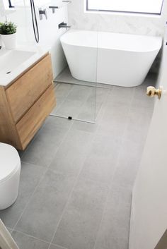 a white bath tub sitting next to a toilet in a bathroom on top of a tiled floor