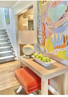 a bowl of fruit sitting on top of a wooden table next to a lamp and stairs