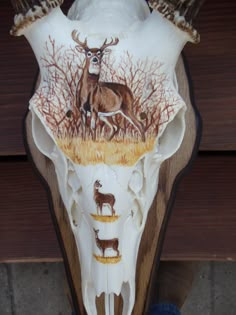 an animal skull with deer and trees painted on it's side, in front of a wooden wall