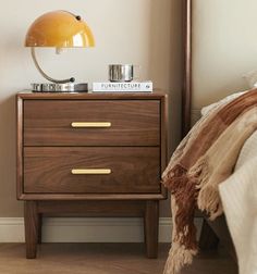 a nightstand with a lamp on top of it next to a bed