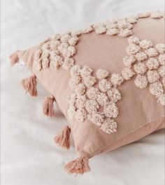 a pink pillow with tassels on it sitting on top of a white bed