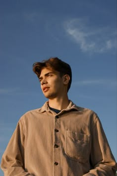 a young man standing in front of a blue sky with his hands folded out to the side