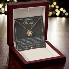 a personalized necklace in a gift box on a table with christmas lights behind it