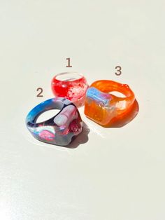 "Colorful and shiny statement rings. Each ring is one of a kind (they have different sizes). You can choose to purchase only one ring, or the three rings in the listing (Prices vary depending on the option you choose). Please select the number of the ring you want or if you would like to take all of them please click the option \"All three rings\". You will receive the exact ring/rings shown in the pictures. Ring 1 Diameter: 17 mm Ring 2 Diameter: 19 mm Ring 3 Diameter: 19 mm" Trendy Resin Ring Jewelry, Trendy Resin Ring, Unique Multicolor Resin Ring, Handmade Multicolor Resin Rings, Trendy Multicolor Resin Rings, Trendy Multicolor Plastic Rings, Unique Clear Resin Ring, Unique Clear Resin Rings, Trendy Plastic Rings As Gifts