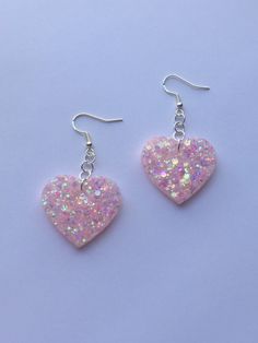 two pink heart shaped earrings with glitter on them are hanging from silver earwires