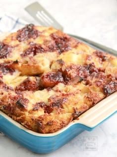 a casserole dish with meat and cheese in it sitting on a table next to a fork