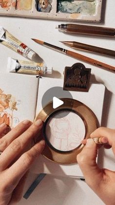 a person holding a magnifying glass in front of some art supplies on a table