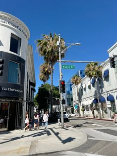 people walking on the sidewalk in front of an intersection with traffic lights and palm trees