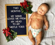 a baby laying next to a sign that says two months my mama loves me from my head to my mistle toes