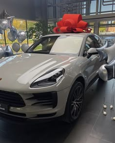 a white porsche cayen with a red bow on its roof in a showroom