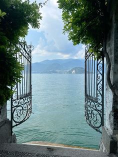 an open gate leading to the water with mountains in the background