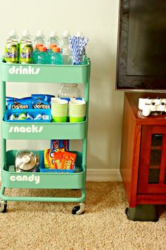 a tv sitting next to a green cart filled with snacks on top of a carpeted floor