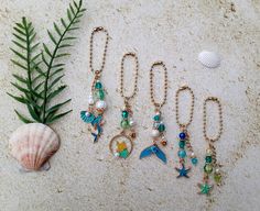 several different necklaces are laying on the sand next to a green plant and seashell