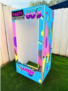 a birthday party in a box sitting on top of the grass next to a fence