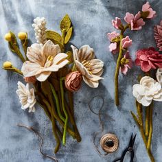 three different types of flowers on a table with yarn and scissors next to them,