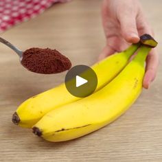 a person holding a spoon with chocolate powder on top of two bananas and another banana in the background