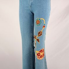 a woman's jeans with embroidered flowers and leaves on the side, in front of a white background