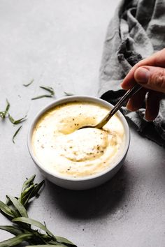 a person dipping something in a bowl with a spoon into the dip and sprinkled with herbs