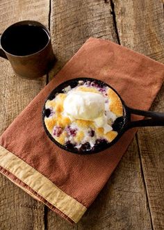 a skillet filled with blueberry cobbler and ice cream next to a cup of coffee