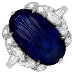 This exceptional Art Deco ring showcases a stunning natural Burmese carved cabochon sapphire, weighing approximately 8.64 carats. The center stone is elegantly complemented by an array of finely set diamonds, including single-cut, marquise, and baguette cuts, creating a harmonious design that enhances the sapphire's beauty. Crafted by hand in the 1920s, this antique ring is a true testament to the artistry of the era. The total approximate diamond weight is 0.60 carats, adding further brilliance Cabochon Sapphire Ring, Antique Cocktail Ring, Art Deco Jewelry Vintage, Sapphire Cocktail Ring, Diamond Pendants Designs, Jewels Rings, Antique Ring, Baguette Cut Diamond, Deco Ring