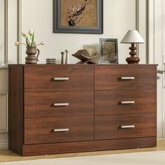 a wooden dresser sitting in a living room next to a lamp and pictures on the wall