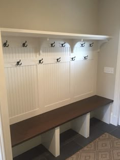 a wooden bench sitting in the middle of a room next to a wall with hooks on it