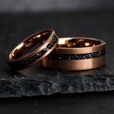 two gold wedding rings with black diamonds on top of each other, sitting on a rock