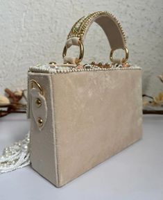 Introducing the Danika Flap Bag, a stunning fusion of bridal elegance and Indian craftsmanship. Hand-beaded with luxurious velvet in enchanting hues of mint, white, and peach, with a beautiful pearl motif, this bag embodies opulence and tradition. Its intricate design, coupled with delicate white suede accents, makes it a standout accessory for brides and lovers of Indian fashion alike. Whether for a wedding ceremony or a cultural celebration, the Danika Flap Bag adds a touch of regal charm to a Luxury Embellished Cream Bags, Luxury Rectangular Box Bag With Pearl Handle, Rectangular Beaded Bag For Reception, Traditional Shoulder Bag With Pearl Embroidery For Reception, Traditional Rectangular Shoulder Bag For Receptions, Beaded Rectangular Bag For Reception, Traditional Rectangular Shoulder Bag For Reception, Luxury Bag With Pearl Embroidery For Reception, Beige Bags With Pearl Embroidery For Reception