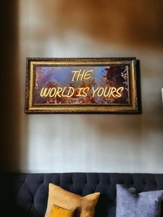 the world is yours sign hangs on the wall above a couch with two yellow pillows