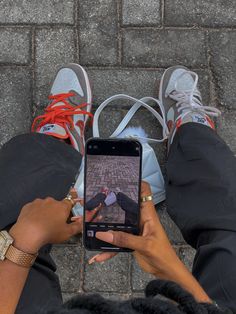 a person holding a cell phone in their hand while sitting on the ground next to some shoes