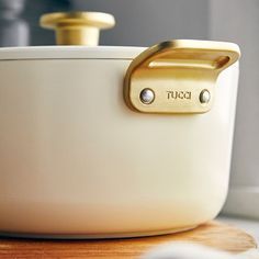 a close up of a white bowl on a wooden table with a gold lid and handles