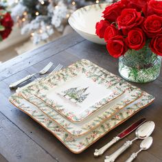 red roses in a glass vase on a table with plates and utensils next to it