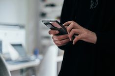 a person holding a cell phone in their hand and looking at it with both hands