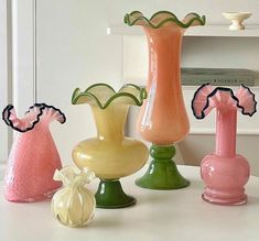 five vases are lined up on a table with one pink and one green, the other yellow