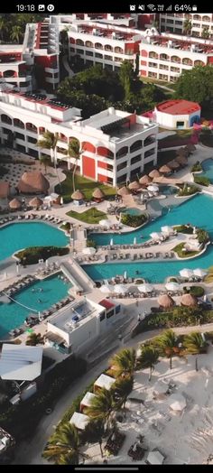 an aerial view of a resort and pool area in the middle of palm trees, with several buildings on either side