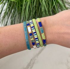 a woman's arm with three bracelets on it and a plant in the background