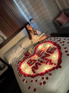 a woman sitting on top of a bed surrounded by candles and rose petals in the shape of a heart