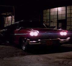 a red car parked in front of a building at night with its hood open and lights on