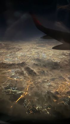 an aerial view of the city lights and clouds in the night sky as seen from an airplane