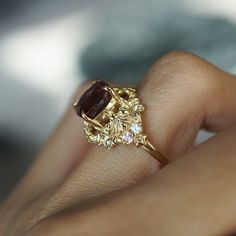 a close up of a person's hand holding a ring with a red stone