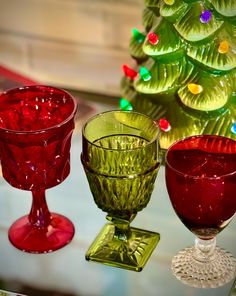 three glass goblets sitting next to a christmas tree