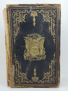 an old book with gold trimmings and ornate designs on the front, sitting on a white surface