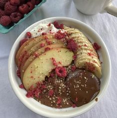 a bowl filled with chocolate, bananas and raspberries next to a cup of coffee