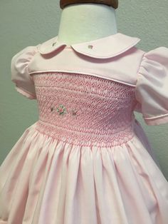 Handsmocked precious pink baby dress adorned with roses.  Peter Pan color and hem of dress also have hand embroidered rosebuds for a precious touch.  Deep bodice smocking, rose floral accent.  Buttons and ties with a bow in the back.  Very full skirt, deep hem.  Machine washable.  Sized for 12-24 months. Fitted Pink Embroidered Smocked Dress, Fitted Pink Smocked Dress With Embroidery, Pink Fitted Dress With Smocked Cuffs, Fitted Pink Smocked Dress, Pink Floral Embroidery Dress For Baptism, Pink Smocked Dress For Baptism, Pink Fitted Smocked Dress For Baptism, Pink Smock Dress For Baptism, Elegant Pink Dress With Smocked Cuffs