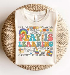 a white t - shirt with the words play is learning written in colorful letters on it